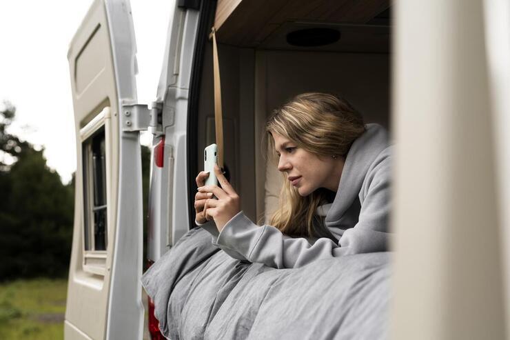 Ragazza sdraiata nel camper che guarda il telefono