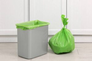 Cestino della spazzatura in cucina con busta verde piena accanto