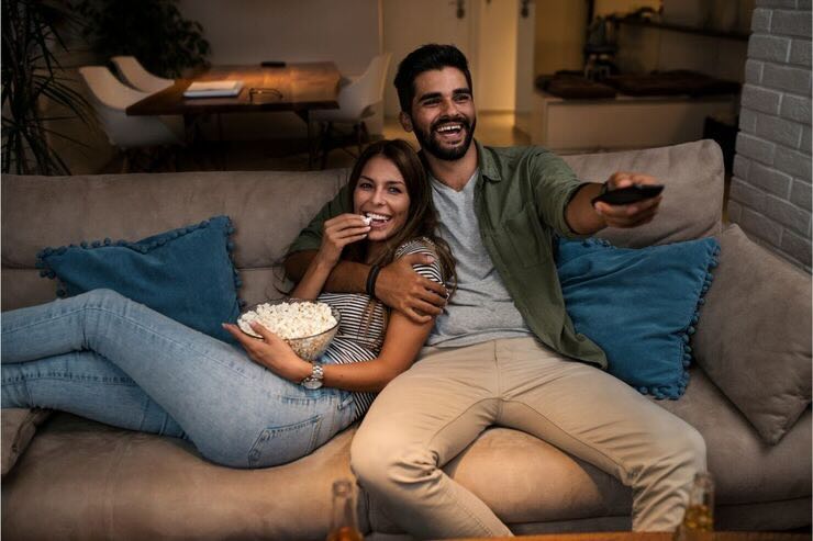 Coppia felice guarda qualcosa in TV sul divano, lei mangia pop corn