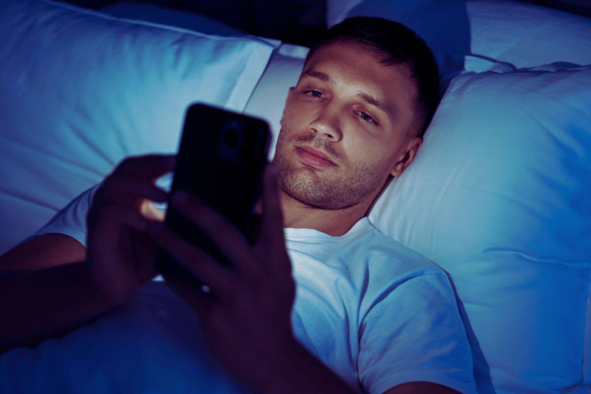 Uomo con cellulare in mano a letto