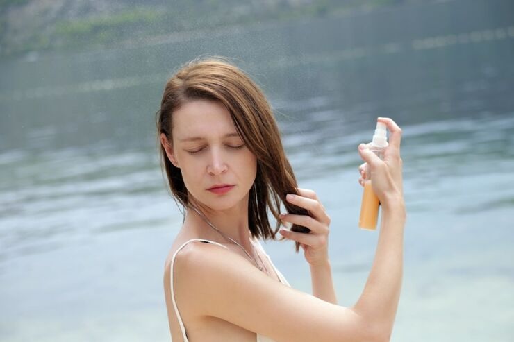 Donna si spruzza spray nei capelli, acqua alle sue spalle 