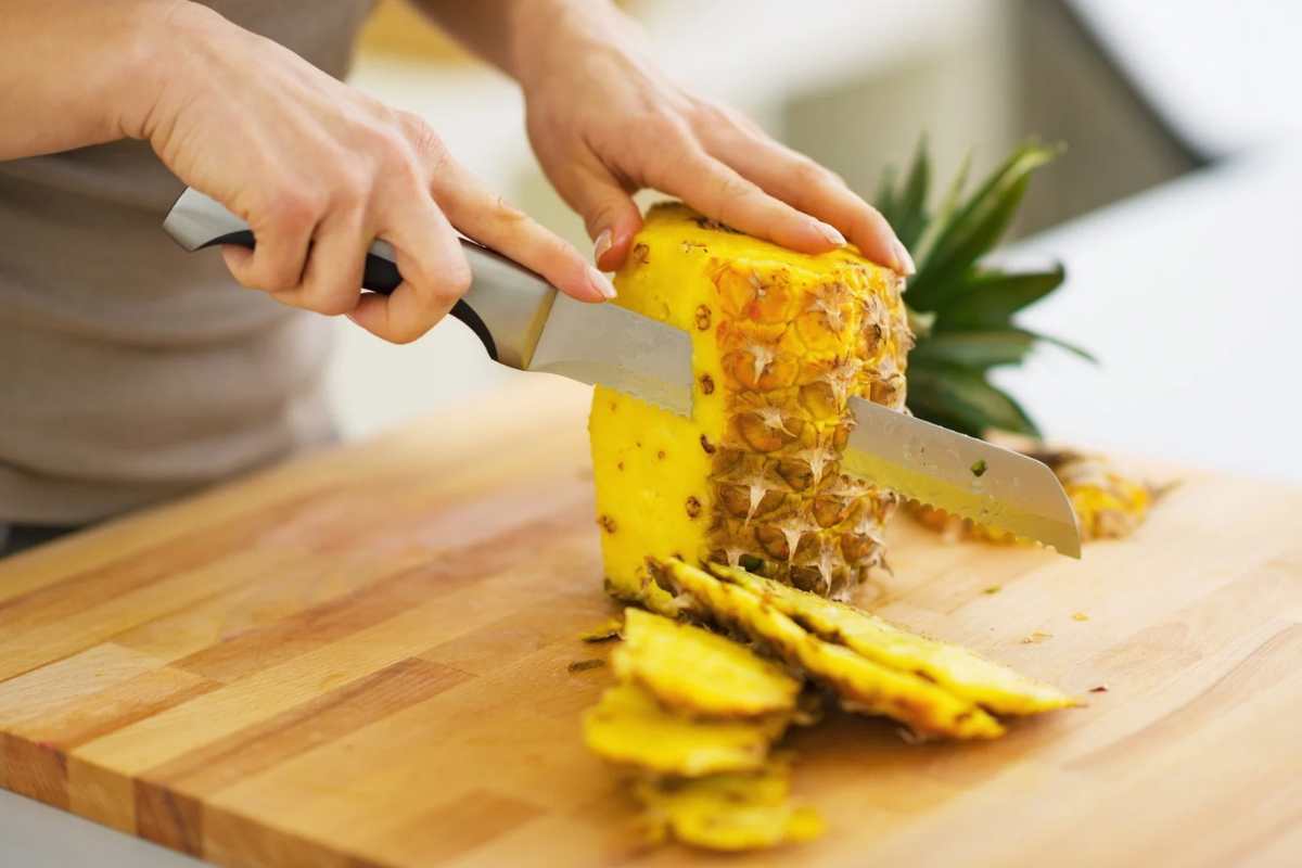 Donna che taglia ananas su un tagliere di legno