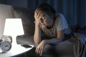 Donna sul letto con mano sul viso, di notte, lumino acceso